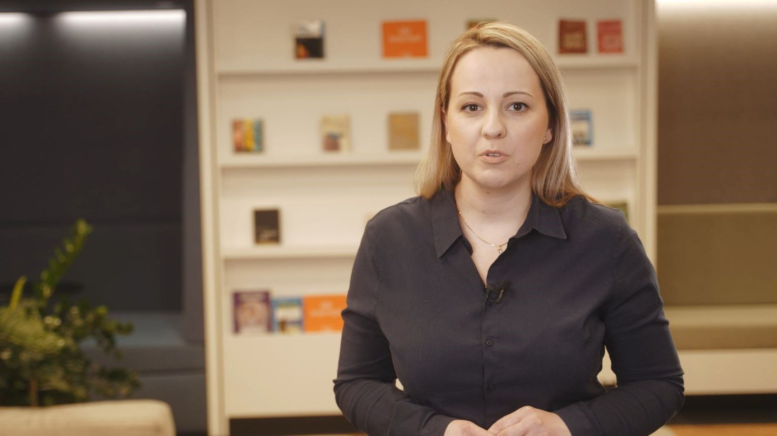 Screen ekranu wideo, w którym kobieta stoi przed kamerą, w tle regał z książkami