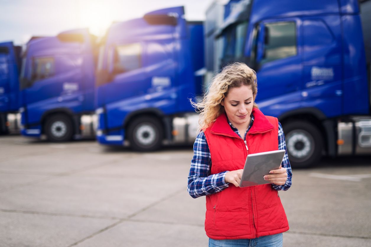przedsiębiorczyni stoi na tle niebieskich samochodów ciężarowych, patrzy w tablet