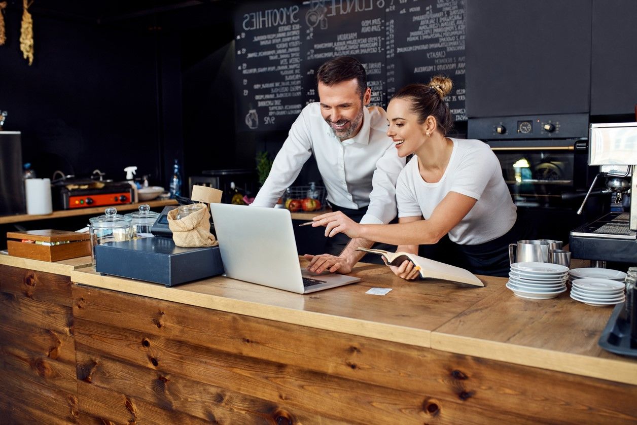 pracownicy kawiarni patrzą w na laptop i uśmiechają się