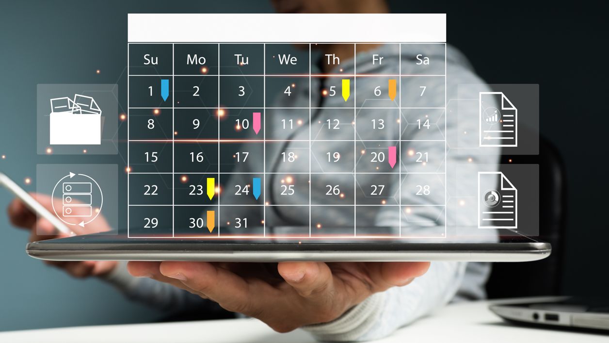 kalendarz z zadaniami do wykonania, w tle laptop i pracownik